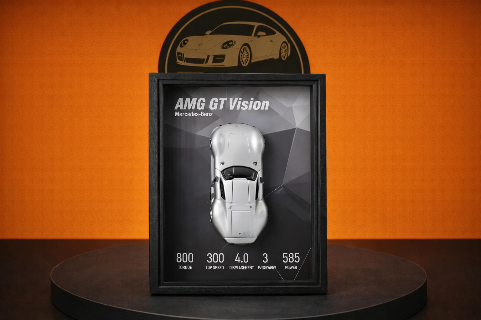 Framed model of silver Mercedes-Benz AMG GT Vision car with specifications on black geometric background, displayed on round black pedestal against orange wall